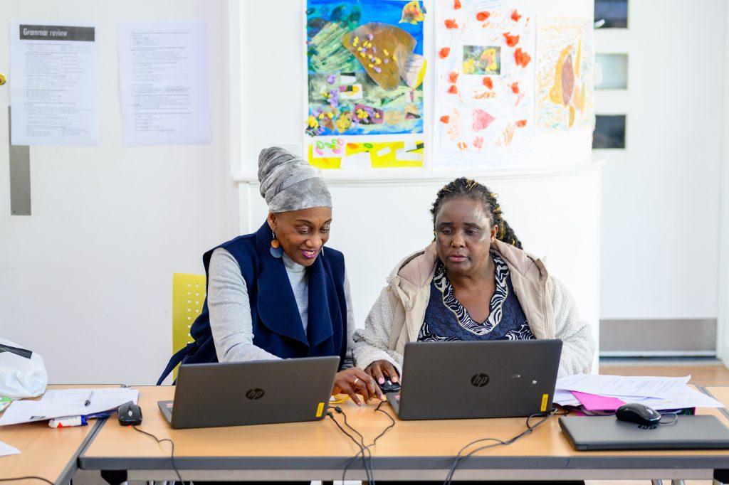 Teacher helping older female student at laptop